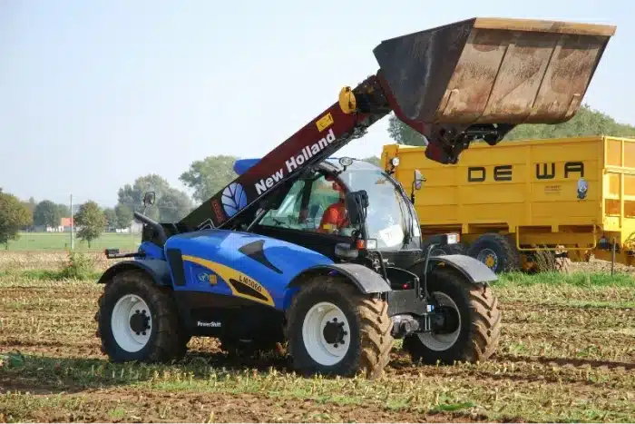 A New Holland telehandler moving dirt in a farm.