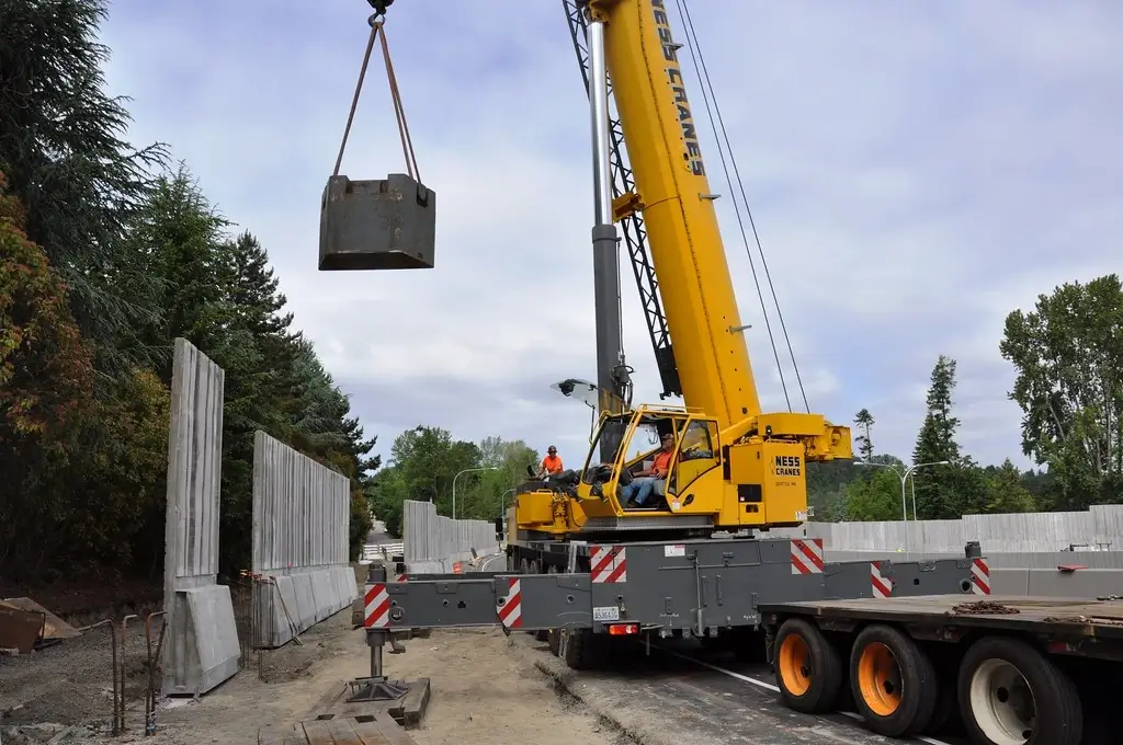 Crane moving heavy block with large trees in background