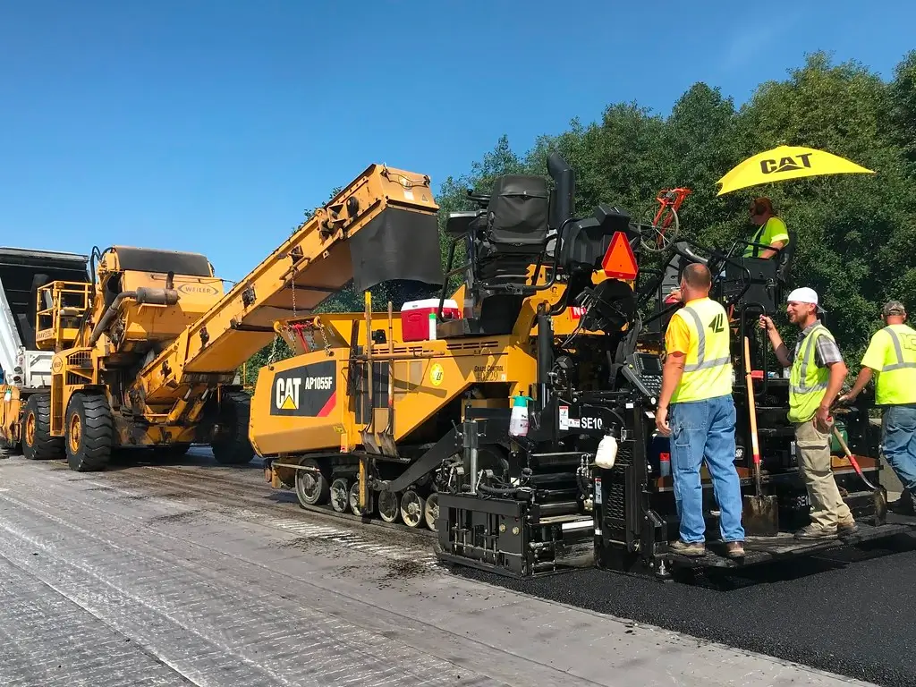 Team of heavy equipment operators using an asphalt paver on a road