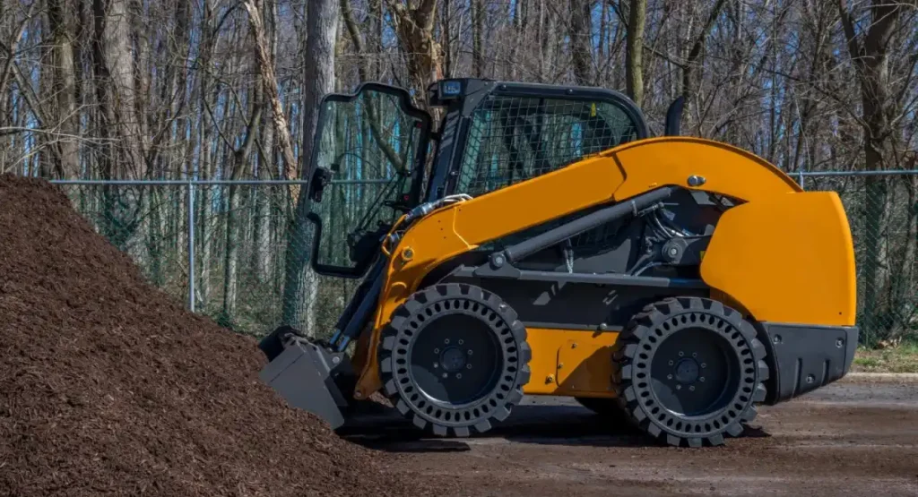 Orange Skid Steer with Solid Tires Near Chain Link Fence